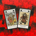 Tarot kortos su atverstu Page of Stakes ir Ten of Stakes motyvais ant raudono nugarėlių fono, detalių iliustracijos