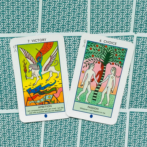 Tarot kortos — dvi atverstos spalvotos kortos (7 Victory/Ambition ir 6 Choice/Passion) ant žalsvo raštuoto fono