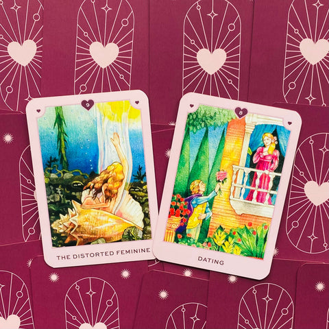tarot kortos su rožiniais kraštais, dvi atviros kortos — "Iškreiptasis moteriškumas" ir "Pasimatymai" ant violetinių nugarėlių