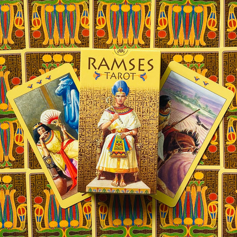 Tarot kortos Ramses geltona dėžutė centre, trys atverstos egiptietiškos kortos ir spalvingas raštuotas galinis fonas