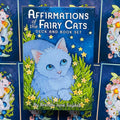 Kortų rinkinys Affirmations of the Fairy Cats su mėlynu dėklu ir knygele, priekinis planas su centrinio balto katino iliustracija ir žvaigždėmis