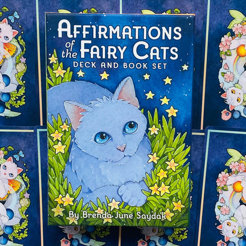 Kortų rinkinys Affirmations of the Fairy Cats su mėlynu dėklu ir knygele, priekinis planas su centrinio balto katino iliustracija ir žvaigždėmis