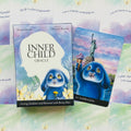 Inner Child orakulas: dėžutė su kortomis ir atversta korta Nr.34 „Inspiration“, mėlynas Benny Blue personažas prieš Laisvės statulos foną