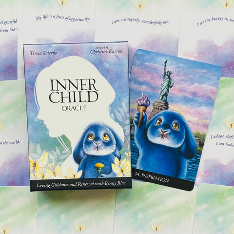 Inner Child orakulas: dėžutė su kortomis ir atversta korta Nr.34 „Inspiration“, mėlynas Benny Blue personažas prieš Laisvės statulos foną