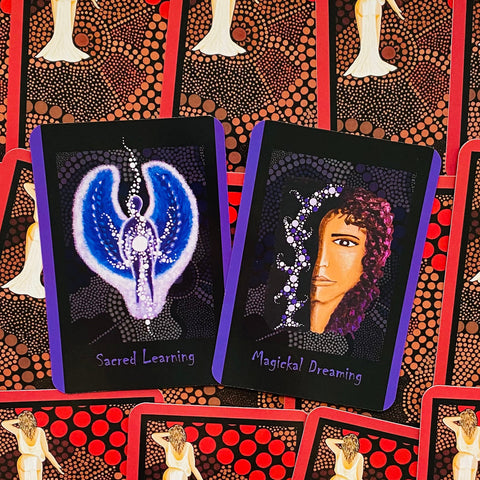 Orakulo kortos: dvi atviros kortos – mėlyna sparnuota Sacred Learning ir portretinė Magickal Dreaming su purpuriniais kraštais ant raudono taškuoto nugarėlio