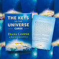 Kortų rinkinys The Keys to the Universe (Diana Cooper) mėlyname dėkle su viena ištrauktą pavyzdine korta, matomas viršelis ir teksto fragmentas