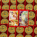 Tarot kortos su raudonomis nugarėlėmis, dvi atviros kortos (6 ir 5 lazdų) su spalvingomis iliustracijomis ir auksiniu ornamentu fonu