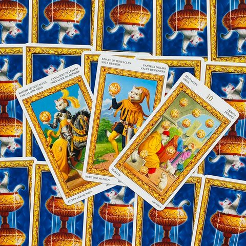 Tarot kortos su kačių motyvais, trys atverstos Pentaklių kortos su auksiniais rėmeliais ant mėlyno galinio fono