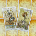 tarot kortos akvarelinės iliustracijos, dvi atviros kortos — svyruojantis katinas (Two of Coins) ir naujos pradžios moteris (Ace of Coins)