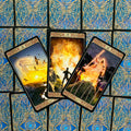 tarot kortos stalo dizaine: trys atvertos kortos su ugnies motyvais ir mėlynomis auksuotomis nugarėlėmis, persidengiančios kampu