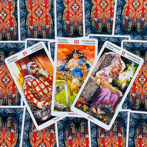 Tarot kortos trys atverstos kortos (Imperatorius, Imperatorė, Vyriausioji kunigė) ant raudno‑mėlyno keltų rašto fono