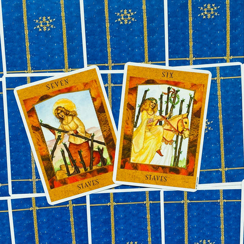 tarot kortos dvi atverstos kortos (Six ir Seven of Staves) su oranžiniais rėmais, išdėstytos ant mėlynos nugarėlės kaip skirtingos variacijos