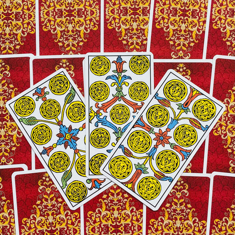 Tarot kortos penketukai: baltos priekinės kortos su geltonais monetų motyvais, trys išdėstytos ant raudonų dekoruotų nugarėlių
