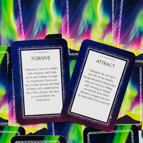 Kortos su šiaurės pašvaistės dizainu, dvi atsiverstos kortos „Forgive“ ir „Attract“ matomos iš arti, rodant tekstus ir kampuotą išdėstymą