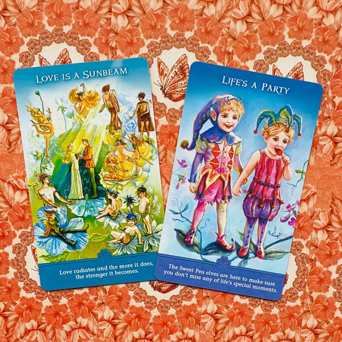 Orakulo kortos su spalvingomis fėjų iliustracijomis — dvi kortos ant rožinio gėlių fono, pabrėžia variantą ir dizainą