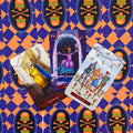 Tarot kortos iliustruotas rinkinys su purpurine‑oranžine kaukolės nugarėle, trys atverstos kortos: riteris, šokanti dama ir dešimt taurų šeimos scena