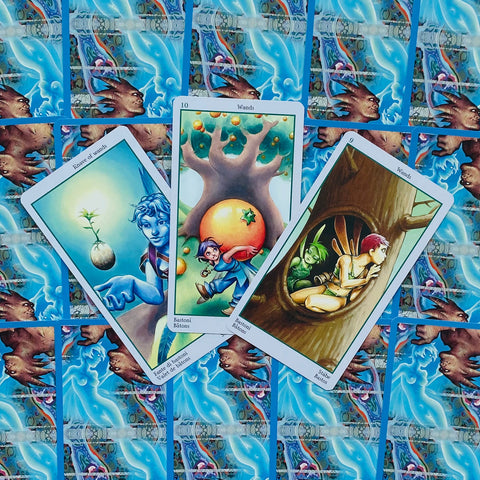 tarot kortos su atverstu trijų kortų išdėstymu, ryškios iliustracijos priekyje ir mėlyni ornamentuoti atgalai