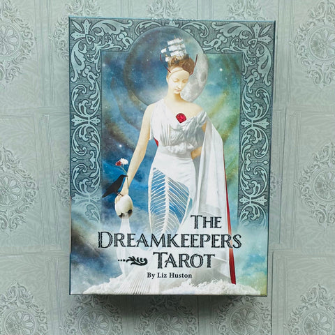 Taro kortos Dreamkeepers — lizdinė pakuotė su baltai apsirengusia figūra, laivo galvute ir paukščiu, laikantį kiaušinį