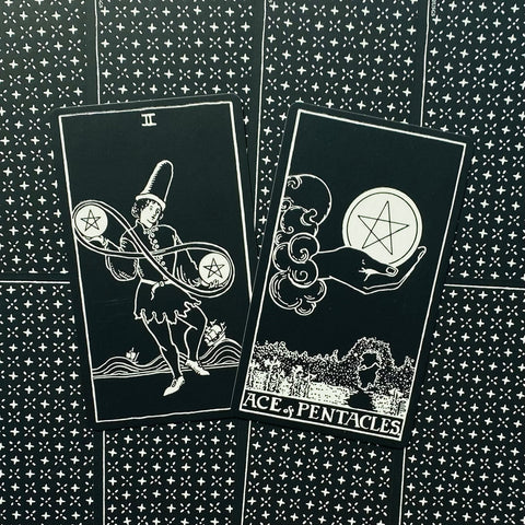 tarot kortos juodai baltos Rider‑Waite stiliaus, dvi kortos (Dviejų pentaklių ir Pentaklių tūzas) ant raštuotos nugarėlės
