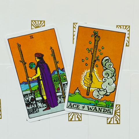 tarot kortos Rider‑Waite komplektas: dvi atviros kortos (Ace of Wands ir Two of Wands) oranžiniame fone, išdėstytos kampuotos