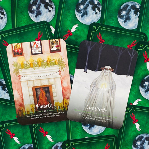 Tarot kortos žaliu nugarėlių dizainu, dvi atverstos kortos Hearth (židinys) ir Gratitude (padėka) su žiemos šventine tematika