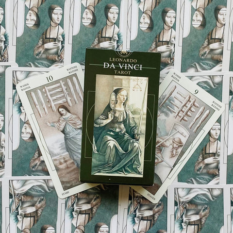 Taro kortų rinkinys Leonardo Da Vinci — tamsiai žalia dėžutė centre, atviros 9 ir 10 lazdų kortos fone
