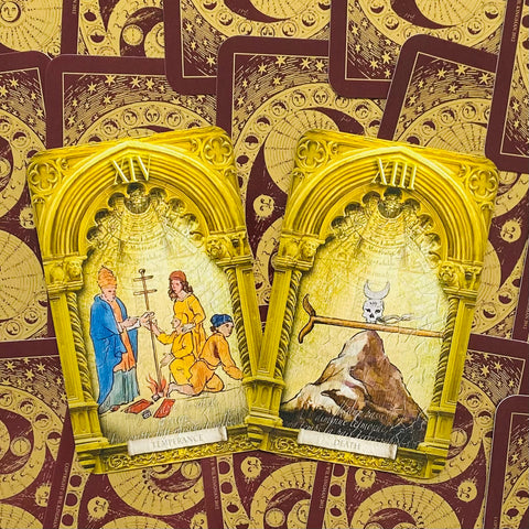 Tarot kortos su aukso arkos rėmeliais — atverstos Didžiosios Arkanos XIV Saikingumas ir XIII Mirtis ant raudono ornamentinio nugarėlių fono