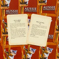 Aussie Affirmations kortelės rudos dėžutės fone, dvi atverstos kortos parodytos iš viršaus su angliškomis afirmacijomis