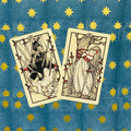 tarot kortos ant mėlyno fono su auksinėmis žvaigždėmis, dvi kreminės kortos su raudonais kardų akcentais ir skirtingomis iliustracijomis