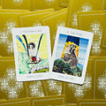Tarot kortos su auksinėmis nugarėlėmis, dvi atverstos kortos (Marie Curie, Joan of Arc) ant ornamentuoto fono kaip komplekto pavyzdys