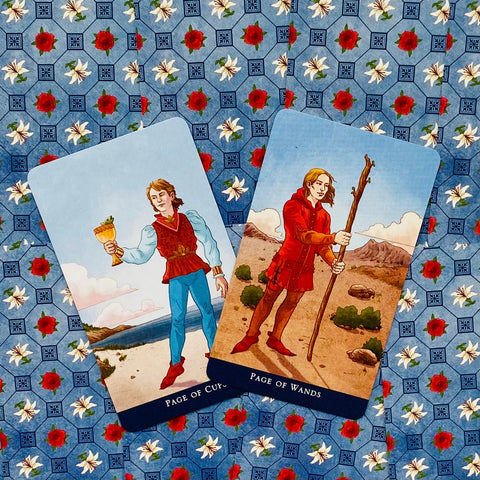 Tarot kortos — Page of Cups ir Page of Wands ant mėlynos gėlių drobės, priekinis artimas planas, ryškios spalvos