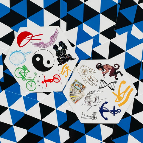 Laikiniai tatuiruočių lipdukai — du šešiakampiai lapeliai su įvairiais simboliais (yin‑yang, tarot, inkaras, dviratis) ant mėlyno‑juodo trikampio fono
