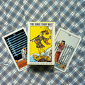 Produkto nuotrauka: The Rider Tarot pocket edition dėžutė priekiniu kampu, šone matomos Devyni ir Aštuoni kardai kortos ant mėlyno languoto fono