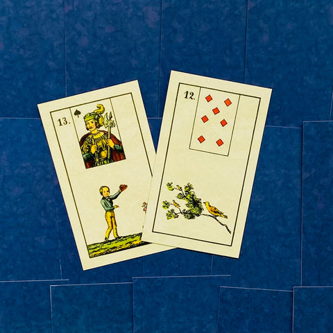 Kortos Lenormand stiliaus rinkinys: dvi kreminės kortos (12 – paukštis, 13 – jaunuolis) guli viena ant kitos ant mėlyno fono