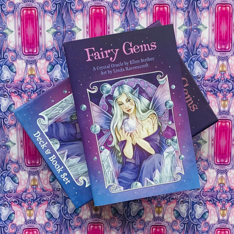 kortų rinkinys Fairy Gems su knygele, violetinės dangos viršelis fėjos iliustracija, padėtas kampu ant raštuoto audinio