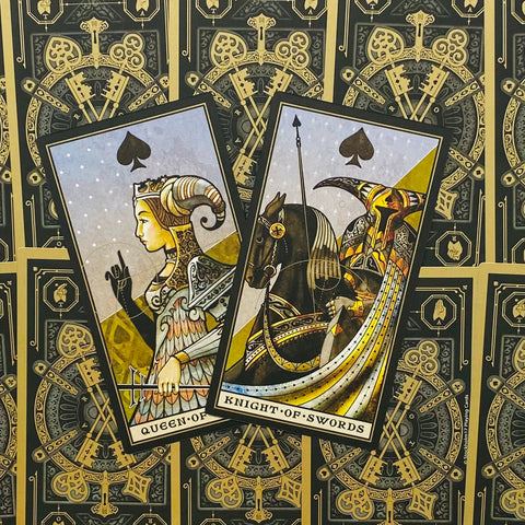 tarot kortos su Queen of Swords ir Knight of Swords žaidimo kortomis, pasvirusios ir arti, ant juodo–auksinio ornamentuoto nugarėlio