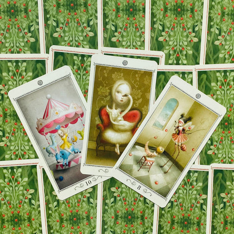 Tarot kortos su meniškais pasakiškais piešiniais — trys atvertos kortos centre ant žalios uogomis raštuotos nugarėlės, rodoma priekio variacija