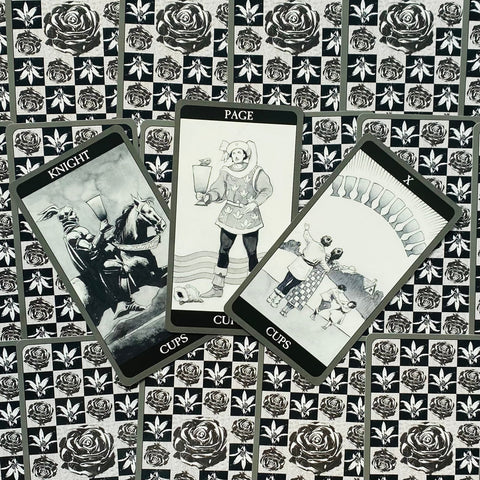 tarot kortos juodai baltos „Cups“ komplektas, trys atverstos kortos ant rožių rašto fono, priekinis kampas