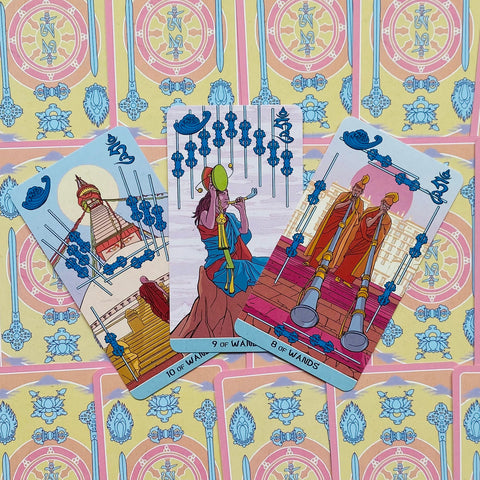 Tarot kortos pasteliniu dizainu — trijų kortų priekiai (8, 9 ir 10 Lazdų) parodyti iš viršaus, matosi unikalus pieštinis motyvas ir nugarėlių raštas