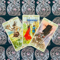 Tarot kortos su akvareliniais piešiniais, trys išdėstytos kortos (raudona suknelė centre) ant ornamentuotos nugarėlės