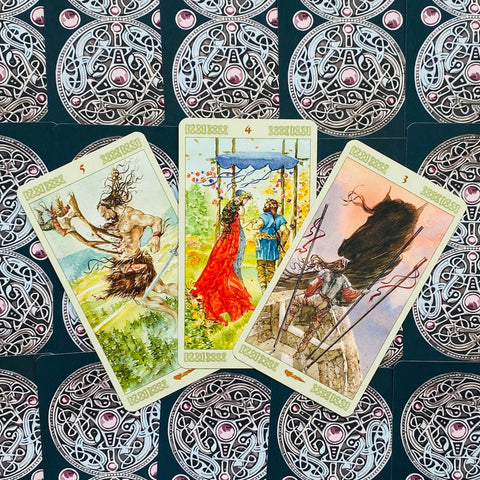 Tarot kortos su akvareliniais piešiniais, trys išdėstytos kortos (raudona suknelė centre) ant ornamentuotos nugarėlės
