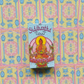 Siddhartha tarot kortos baltai-mėlyname dėkle su sėdinčio Budos iliustracija, centre ant pastelinio kortų fono