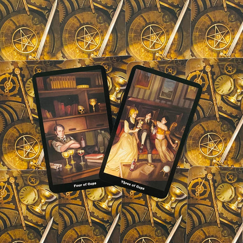 tarot kortos dviejų atverstų kortų – Four of Cups ir Three of Cups ant auksinio mechaninių ratų nugarėlės fono