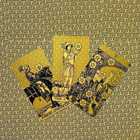 Tarot kortos su aukso folijos pentaklėmis, trys kortų variantai išdėstyti vėduokle ant auksinio mozaikinio fono