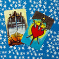 tarot kortos – ryškūs peiliai ir įmerktas širdies motyvas ant mėlyno žvaigždėto nugarėlio, skirtingi priekiai