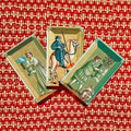 Tarot kortos — trijų istorinių iliustruotų kortų rinkinys ant raudono lelijos raštuoto fono, plokščias išdėstymas