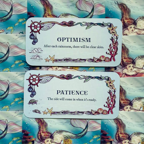 Inspiracinės kortelės su jūros motyvais, pastelinė mėlyna fone, dvi kortelės „Optimism“ ir „Patience“ išdėstytos viena virš kitos