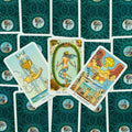 Tarot kortos Rider–Waite stiliaus komplektas su trimis atverstomis kortomis (XXI, XX, taurės tūzas) ant žalsvai tamsios nugarėlės, fotografuotos iš viršaus