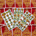 Tarot kortos su raudonomis nugarėlėmis ir auksiniu ornamentu, trys atverstos taurės kortos fane su ryškiomis spalvotomis detalėmis