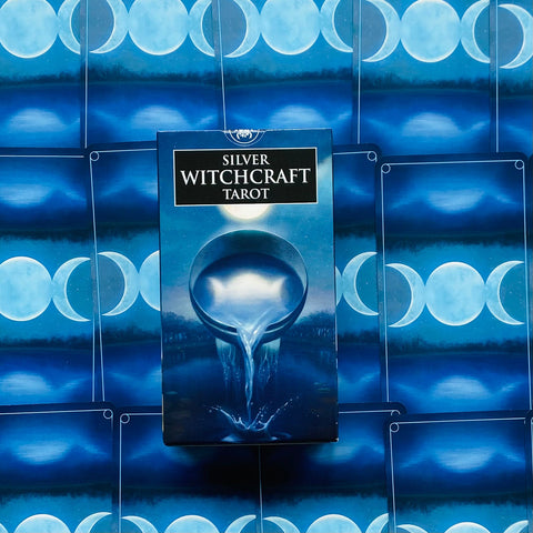 Tarot kortos Silver Witchcraft supakuotos mėlyname dėkle, centre ant išskleistų mėlynų kortų nugarėlių su trijų mėnulių motyvu
